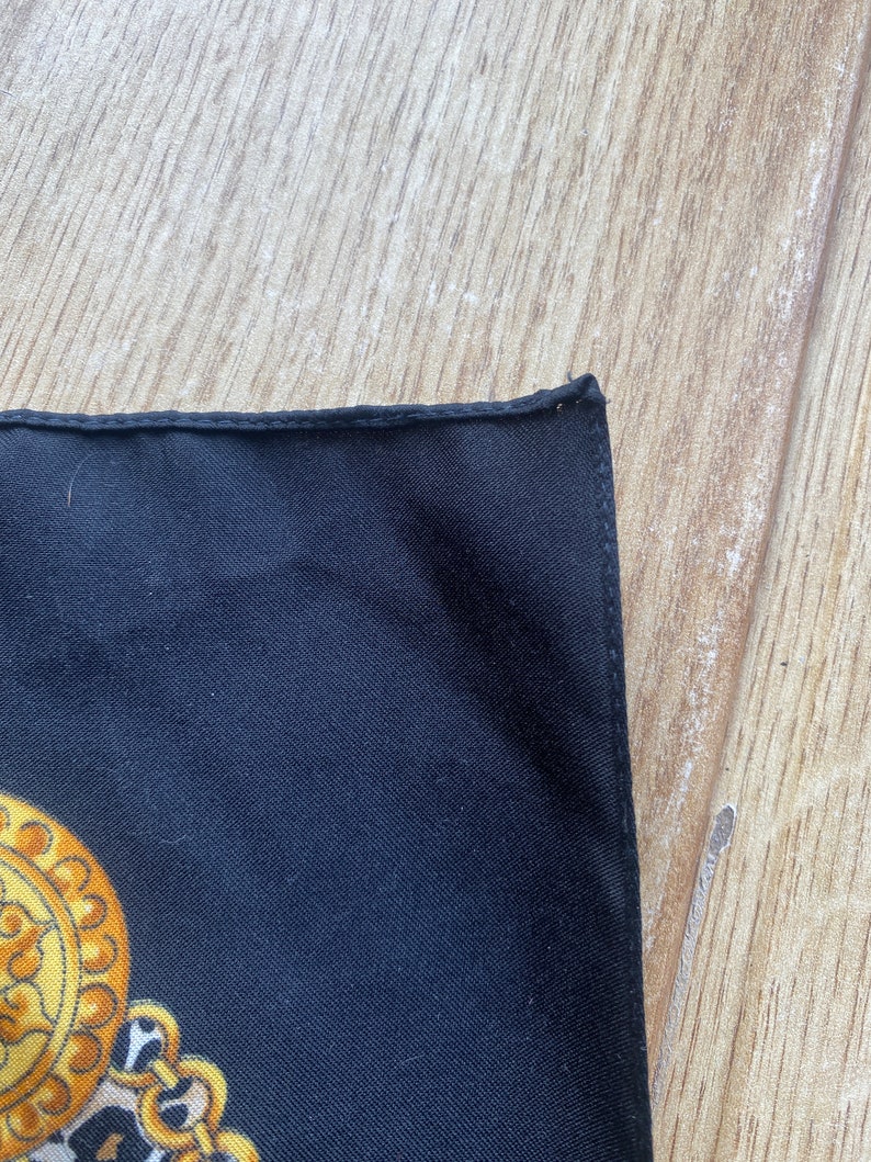 May include: A black silk scarf with a gold and yellow chain pattern. The scarf has a finished edge.