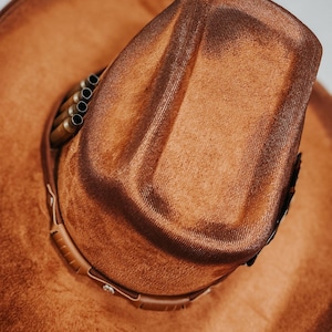May include: A brown cowboy hat with a band and a row of metal bullet casings on the crown.