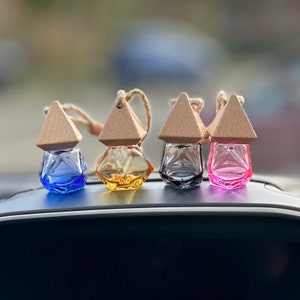 May include: Four small glass bottles with wooden tops and string hangers. The bottles are filled with different coloured liquids and have a geometric shape. The bottles are arranged in a row on a black surface.