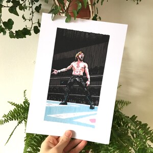 Puede incluir: Una ilustración en blanco y negro de un luchador en un ring de lucha libre. El luchador lleva pantalones cortos negros y un cinturón de lucha libre negro. El luchador levanta los brazos en el aire y tiene una expresión decidida en su rostro.