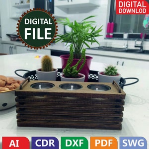May include: A wooden candle holder with three slots for tea lights. The holder is made of stacked wooden slats and has a brown finish. The holder is sitting on a white countertop with a black tray and three small potted plants.