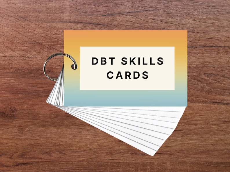 May include: A set of DBT Skills Cards in a ring binder with a yellow to blue gradient cover. The cover has the text "DBT SKILLS CARDS" in black.