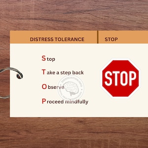May include: A white card with the words "Distress Tolerance" and "STOP" in brown text at the top. The card has a list of four steps to help manage distress: "Stop", "Take a step back", "Observe", and "Proceed mindfully". A red stop sign with the word "STOP" in white text is on the right side of the card.