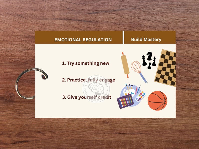 May include: A brown card with the text "Emotional Regulation" and "Build Mastery" on it. The card has three steps listed: "Try something new", "Practice, fully engage", and "Give yourself credit". The card also has illustrations of a rolling pin, whisk, paintbrushes, a chessboard, and a basketball.