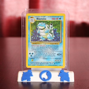 May include: A clear plastic case with a blue and white Pokemon card inside. The card features a blue and white Blastoise Pokemon with the text "Blastoise 100 HP" and "Shellfish Pokemon Length: 6'7" Weight: 189 lbs."