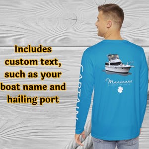 May include: A light blue long-sleeve shirt with a boat graphic on the back. The shirt includes the text "CAPTAIN" on the left sleeve and the text "Includes custom text, such as your boat name and hailing port" on the left side.