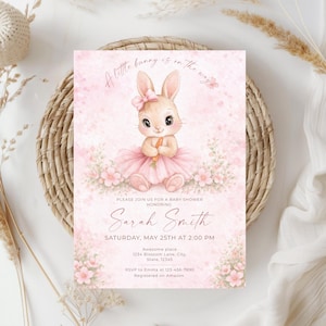 Può includere: Invito per baby shower rosa con un'illustrazione di un coniglietto con un tutù che tiene una carota. Il testo recita "A little bunny is on the way", con i dettagli dell'evento: nome dell'invitato d'onore, data, ora e luogo. Decorato con elementi floreali.