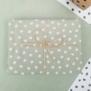 May include: A sage green gift box with white polka dots wrapped with twine and tied with a bow.