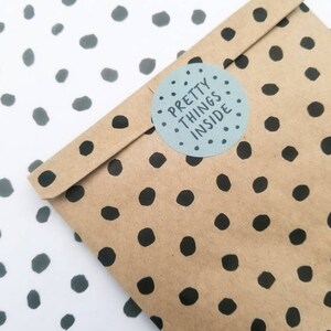 May include: A brown paper bag with a black polka dot pattern. A white circle sticker with black text reads "PRETTY THINGS INSIDE".