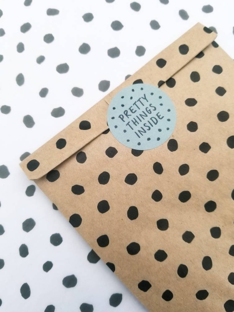 May include: A brown paper bag with a black polka dot pattern. A white circle sticker with black text reads "PRETTY THINGS INSIDE".