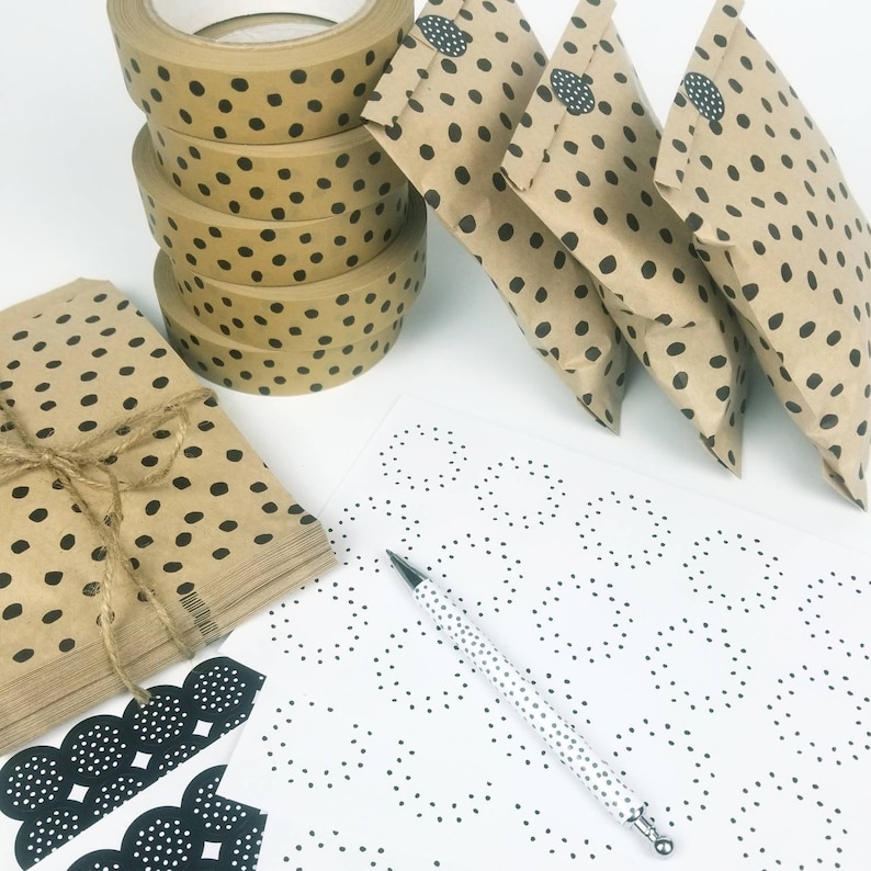 May include: A set of four brown paper gift bags with black polka dots. The bags are arranged in a row, with the largest bag in the back and the smallest bag in the front. The bags are all tied with twine. There is a roll of brown packing tape with black polka dots in the background.