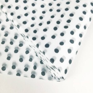 May include: White tissue paper with a black polka dot pattern. The tissue paper is folded in half and the polka dots are visible on both sides.