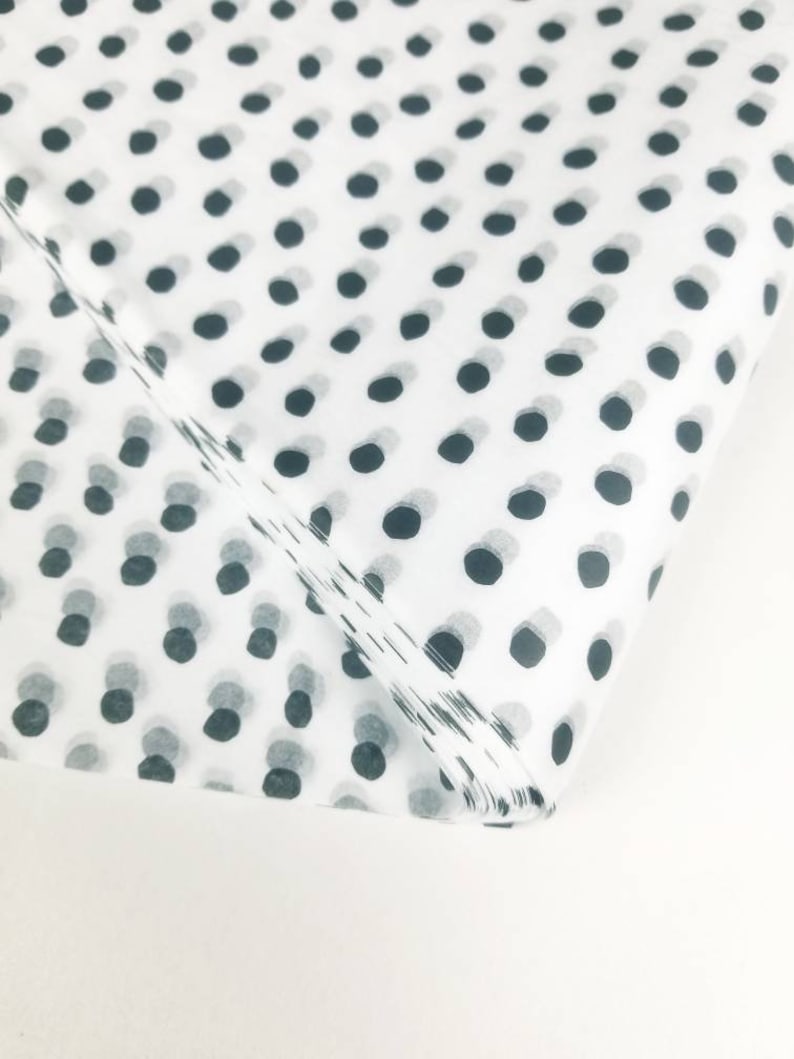 May include: White tissue paper with a black polka dot pattern. The tissue paper is folded in half and the polka dots are visible on both sides.