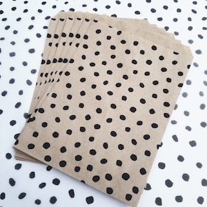 May include: A stack of brown paper bags with a black polka dot pattern. The bags are folded and stacked on top of each other.