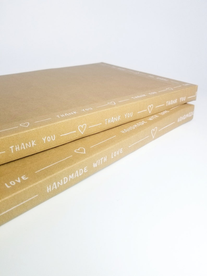 May include: Two brown cardboard boxes stacked on top of each other. The boxes are decorated with white hearts and the text "Thank You" and "Handmade with Love".