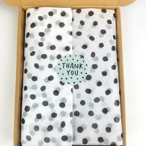 May include: A cardboard box with a white tissue paper lining. The tissue paper has a black and white polka dot pattern. A sticker with the text "THANK YOU" is on the tissue paper.