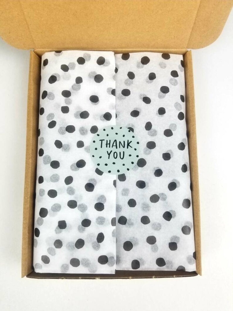 May include: A cardboard box with a white tissue paper lining. The tissue paper has a black and white polka dot pattern. A sticker with the text "THANK YOU" is on the tissue paper.
