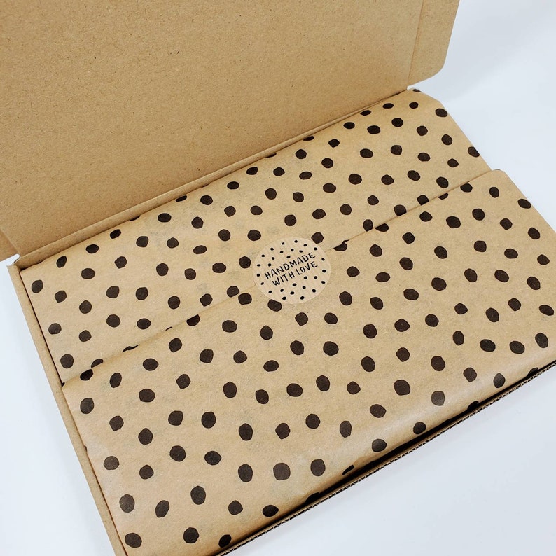 May include: A brown cardboard box with a lid open, revealing brown paper with black polka dots. The paper has a round sticker that says "Handmade with Love".
