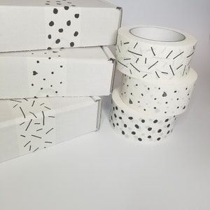 May include: Four rolls of white washi tape with black and white geometric patterns. The patterns include dots, lines, and a combination of dots and lines.