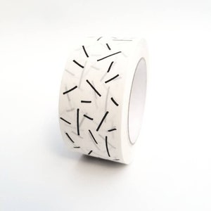 May include: A roll of white washi tape with a black and white geometric pattern of thin lines.