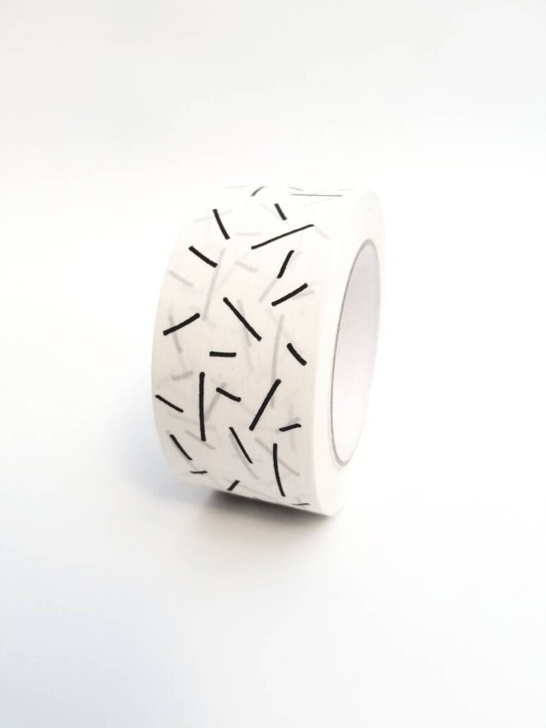 May include: A roll of white washi tape with a black and white geometric pattern of thin lines.