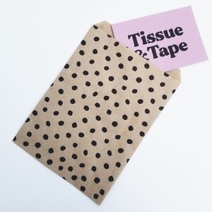 May include: A brown paper bag with black polka dots, partially open to reveal a pink card with the text "Tissue & Tape" in black.