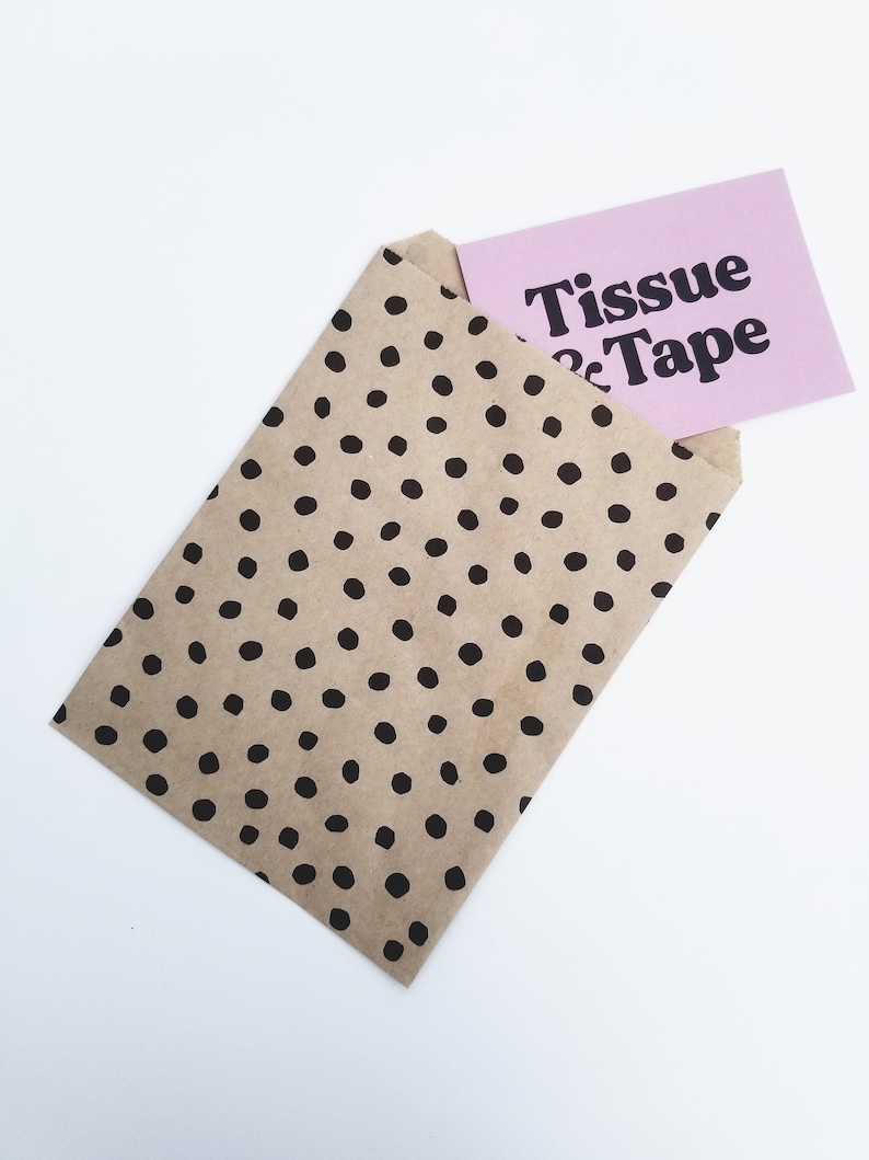 May include: A brown paper bag with black polka dots, partially open to reveal a pink card with the text "Tissue & Tape" in black.