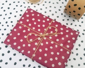 May include: A red gift wrap with white polka dots tied with twine. The gift wrap is on a white background with black polka dots.