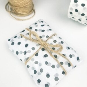 May include: A small gift wrapped in white paper with black polka dots. The gift is tied with twine and a bow.