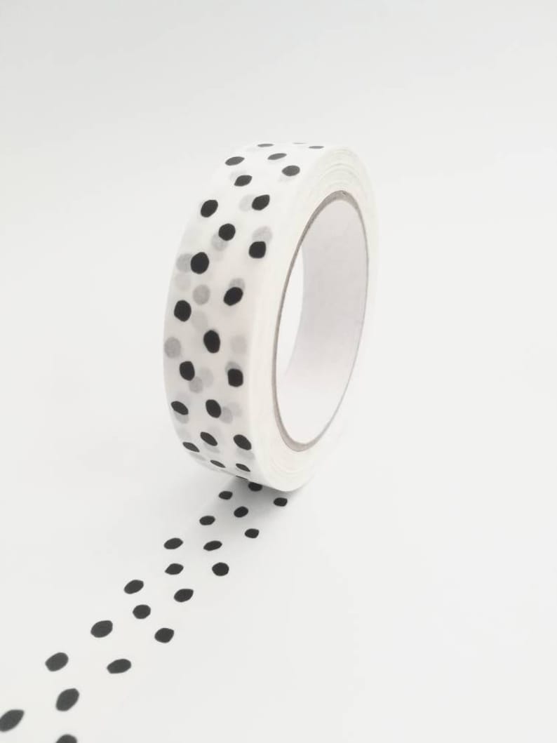 May include: A roll of white washi tape with a black polka dot pattern. The tape is unrolled and the polka dots are visible.