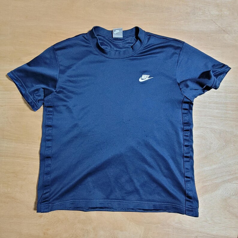 Puede incluir: Una camiseta azul marino de manga corta con un logotipo blanco de Nike en la parte delantera.