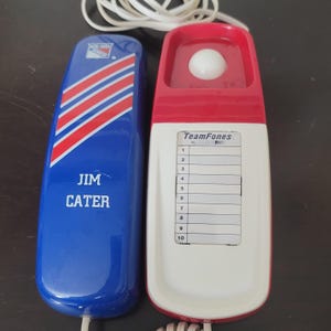 以下が含まれることがあります： 2つのヴィンテージTeamFones電話。1つはニューヨークレンジャーズのロゴと「JIM CATER」という名前が入った青色です。もう1つは赤と白で、番号のリストが付いています。どちらもコードが付いています。