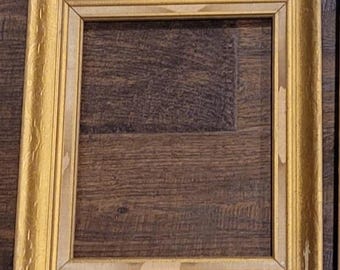 May include: A rectangular picture frame with a gold-toned finish and a textured, ornate border. The frame features a smooth inner edge and shows visible signs of wear, including small areas where the gold finish has chipped away to reveal the base.
