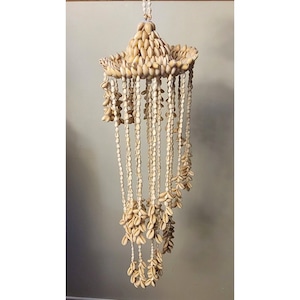 May include: A white seashell wind chime with multiple strands of shells hanging from a large, round, seashell top.