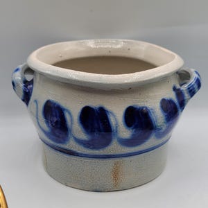 Puede incluir: Una olla de cerámica blanca con diseños de espiral azul y blanco y dos asas. La olla está vidriada y tiene un aspecto rústico.