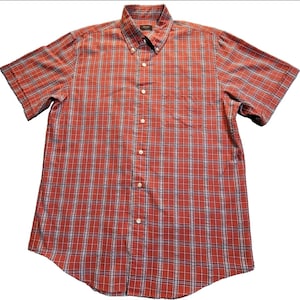 May include: A short-sleeved shirt with a red and white plaid pattern and blue accents. It features a button-down collar and a chest pocket. The fabric is likely cotton or a similar material. The shirt is designed for casual wear.