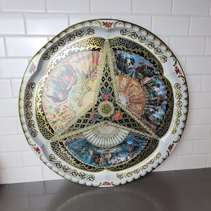 May include: A round, white metal tray with a gold rim and intricate floral designs. The tray is decorated with three colorful images of fans, each with a different design.