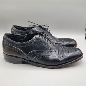 May include: A pair of black leather lace-up shoes with wingtip detailing. The shoes have a brogue pattern and a polished finish.