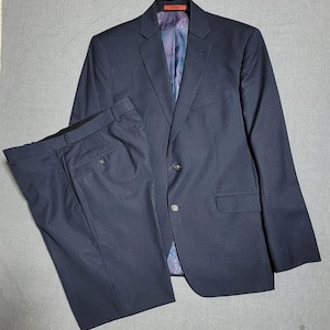 May include: A navy blue suit set, including a blazer and matching trousers. The blazer has a two-button closure and a patterned lining. The trousers have a classic design. The suit is made of a textured fabric.