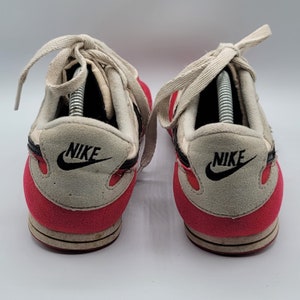 May include: A pair of red and white Nike sneakers with black accents and the Nike logo on the side. The shoes have white laces and a white tongue.