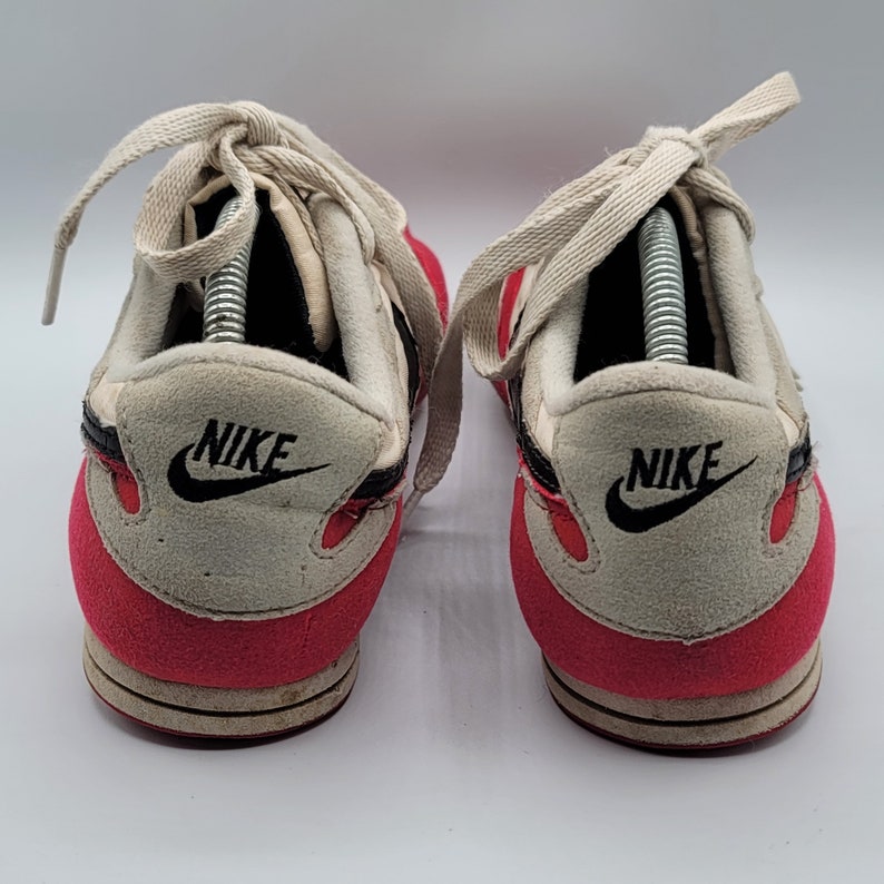 May include: A pair of red and white Nike sneakers with black accents and the Nike logo on the side. The shoes have white laces and a white tongue.