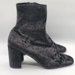 Peut inclure: Une paire de bottines en velours noir. Les bottines ont un bout arrondi et un talon bloc. La tige de la botte est mi-haute et il y a une fermeture éclair sur le côté. Les bottines sont en velours doux et moelleux.