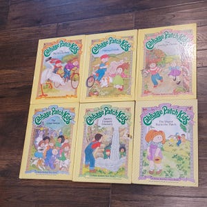 Könnte beinhalten: Eine Sammlung von sechs Cabbage Patch Kids-Bilderbüchern mit gelben Einbänden, die illustrierte Szenen mit Charakteren in verschiedenen Außenumgebungen zeigen. Jedes Buch trägt den Titel und das Parker Brothers Story Book-Logo.