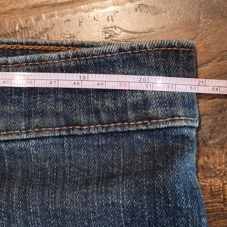 Puede incluir: Primer plano de la cintura de un par de pantalones vaqueros azules con una cinta m&eacute;trica blanca que muestra 50 pulgadas.