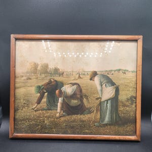May include: A framed print depicting three figures harvesting wheat in a field. The artwork features a muted color palette with brown, green, and beige tones. The wooden frame adds a rustic touch to the pastoral scene.