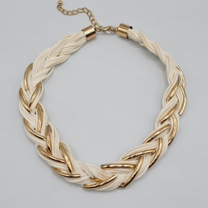 May include: A white braided necklace with gold accents. The necklace is made of a woven cord with gold metal accents.