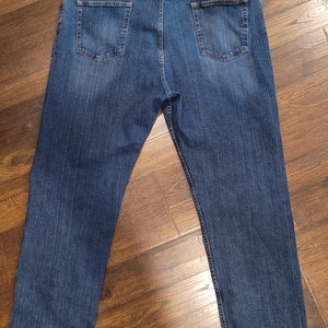 Puede incluir: Un par de pantalones vaqueros azules con un parche de cuero marr&oacute;n en el bolsillo trasero derecho que dice "Wrangler, Authentic Western Wear".