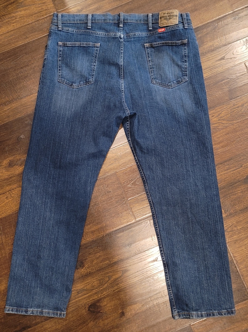 Puede incluir: Un par de pantalones vaqueros azules con un parche de cuero marr&oacute;n en el bolsillo trasero derecho que dice "Wrangler, Authentic Western Wear".