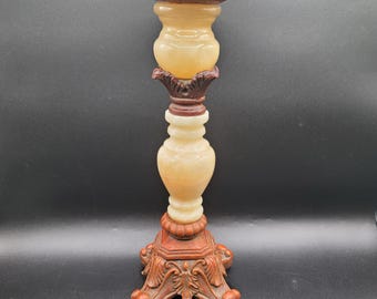 May include: Ornate candle holder with a carved base and a light-colored, bulbous body. The base and accents are a reddish-brown, while the main body has a creamy, translucent appearance. The top is a flat, circular surface.