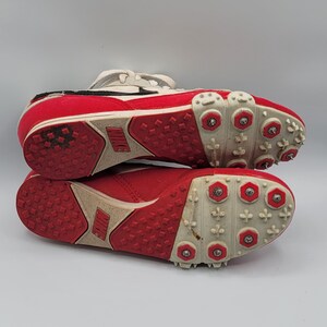 May include: A pair of red and white track shoes with metal spikes on the soles. The shoes have a white Nike logo on the side.
